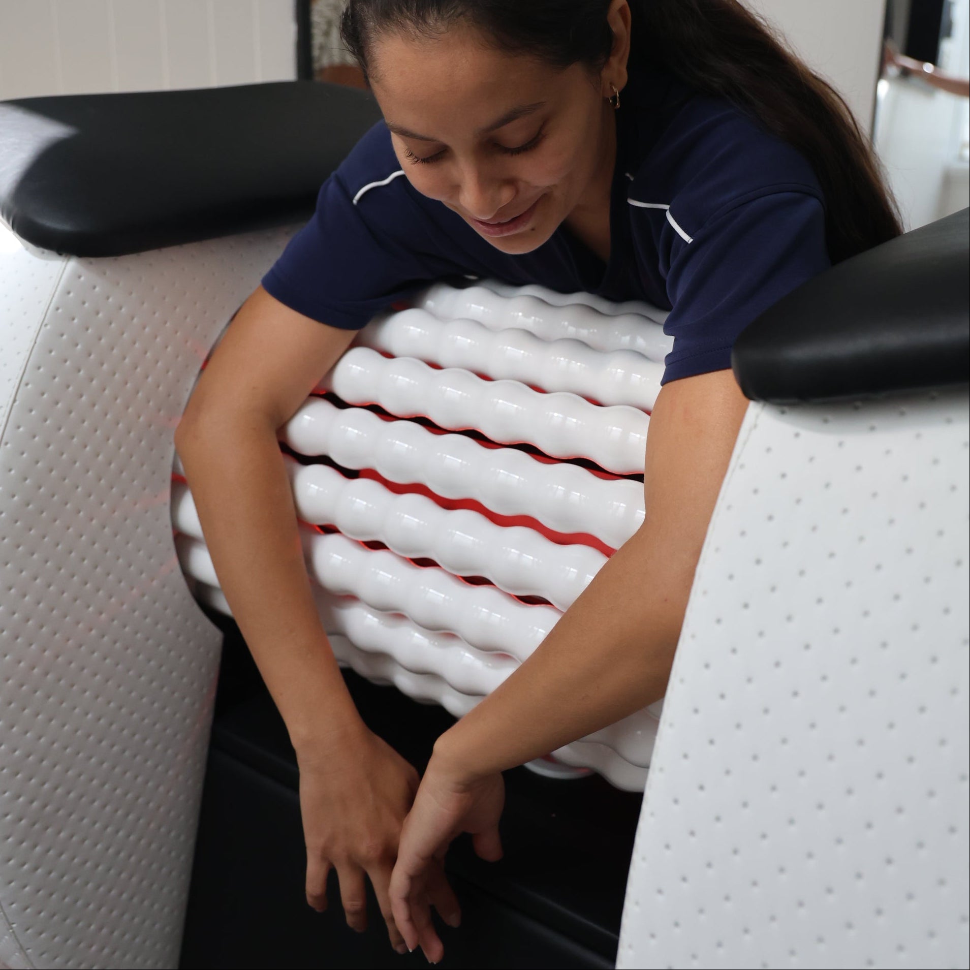 Person using a white body roll massage machine in a modern studio setting